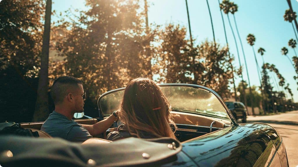 two people driving down a palm-tree-lined road in a convertible car in Los Angeles